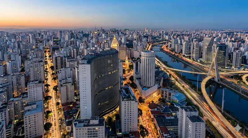 Aerial view of a Brazilian city skyline at sunset with warm orange sky over high-rise buildings